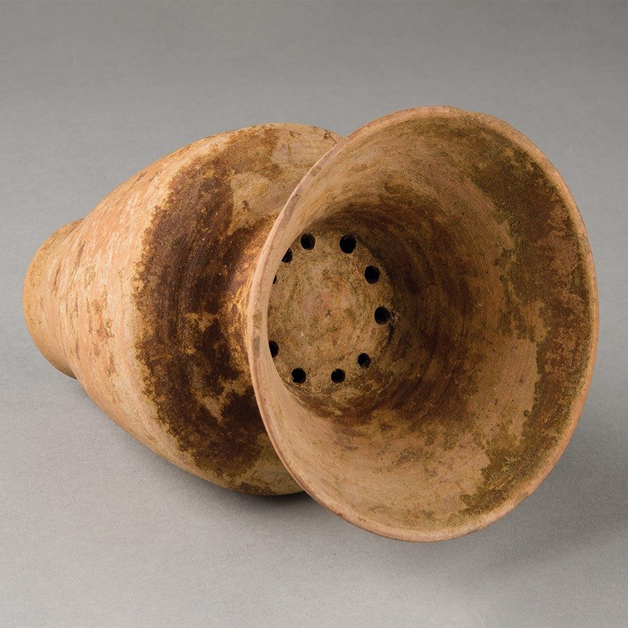 Buff-colored clay water filter shaped like an amphora. It has a circle of holes serving as a passageway between the top and bottom parts of the vessel.