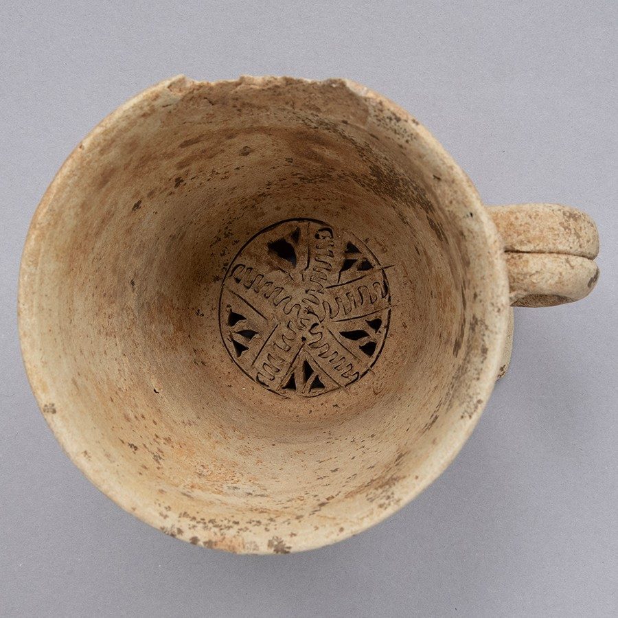 Buff-colored clay water filter with a five-sided geometric shape radiating out from the center. The vessel also has a small handle.