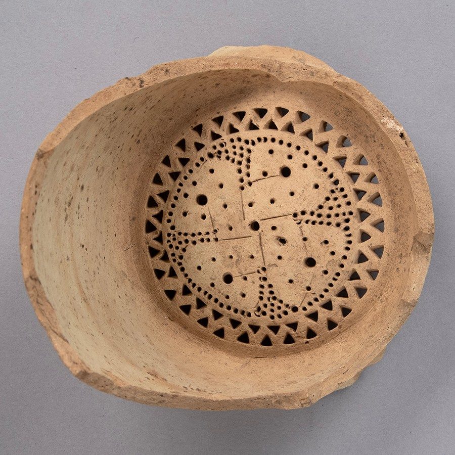 Buff-colored clay water filter with a four-petaled flower at the bottom.