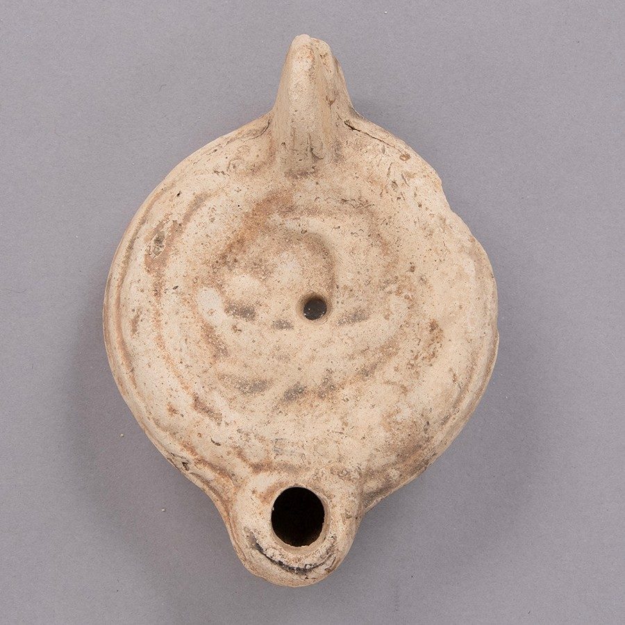 Oil lamp fashioned of light tan clay with the faint impression of a boat shaped into the surface.
