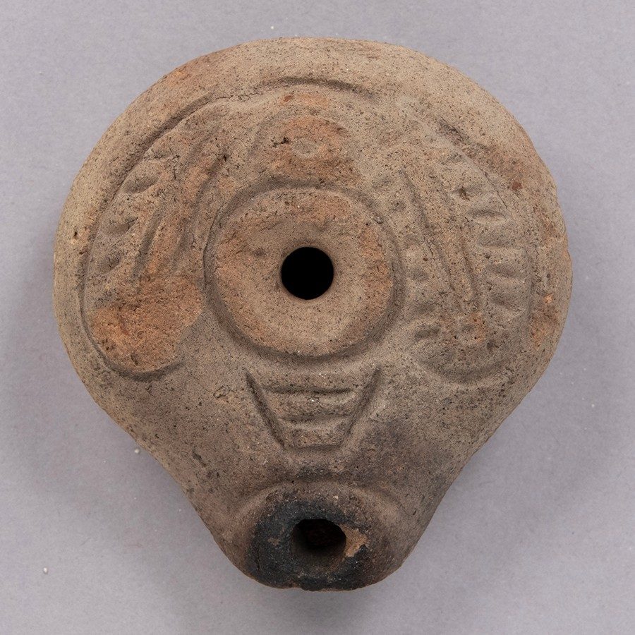 Tan, squat terracotta oil lamp with geometric patterns on its surface.