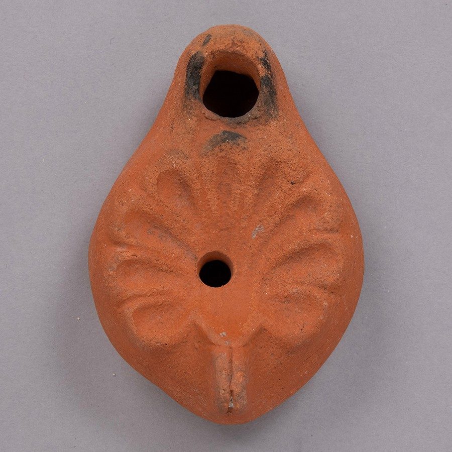 Red-orange terracotta oil lamp with a many-petaled flower impressed into its surface.