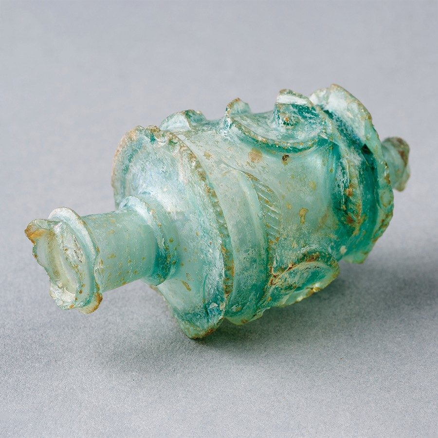 Light teal glass object with a narrow spout and a body cut with geometric patterns.