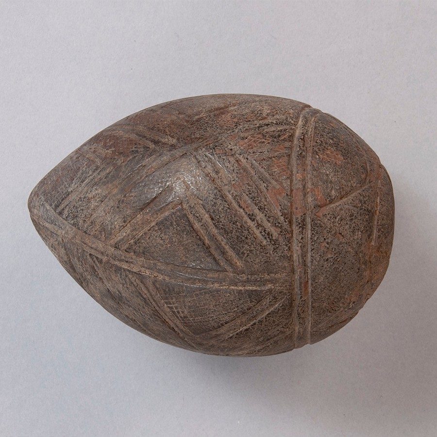 Egg-shaped, pointed husk of a coconut carved with lines and geometric shapes.