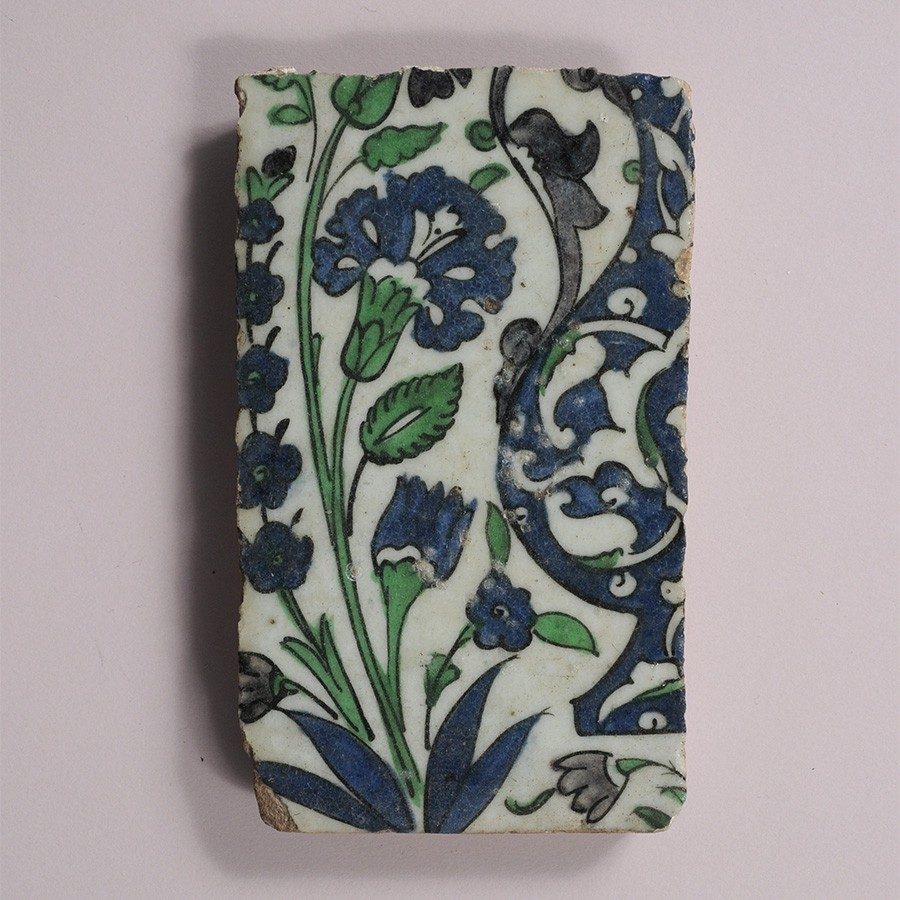 Rectangular tile decorated with images of green and blue swirling vines, leaves, and flowers against a white background.