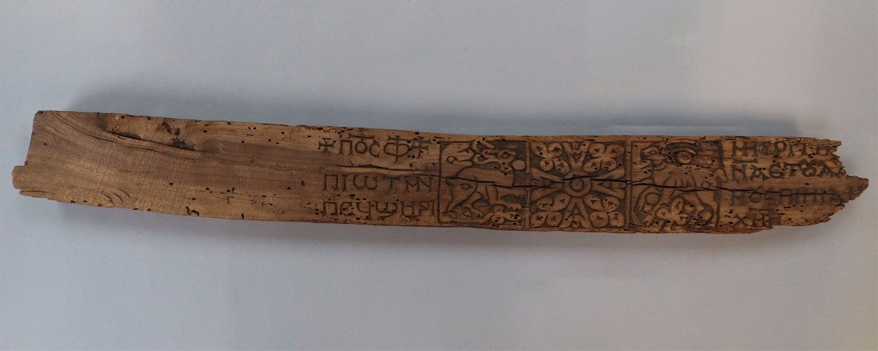 Long, rectangular wooden relief panel with square blocks of carvings of inscriptions, a hare, a Greek cross, and a gazelle.