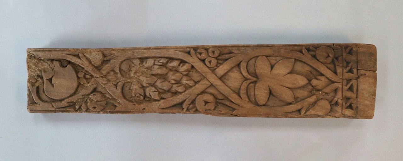 Long, rectangular wooden relief panel decorated with carvings of vines and leaves.