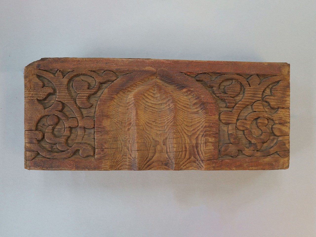 Rectangular wooden relief panel carved with a beveled arch surrounded by swirling vines.