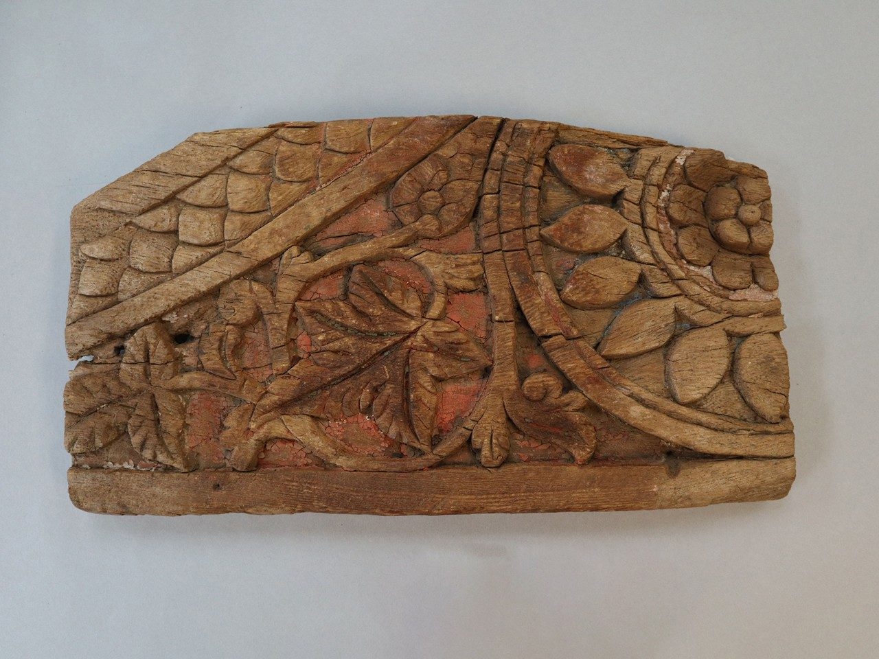 Rectangular wooden relief panel decorated with carvings of flowers, leaves, and vines and with traces of red paint.