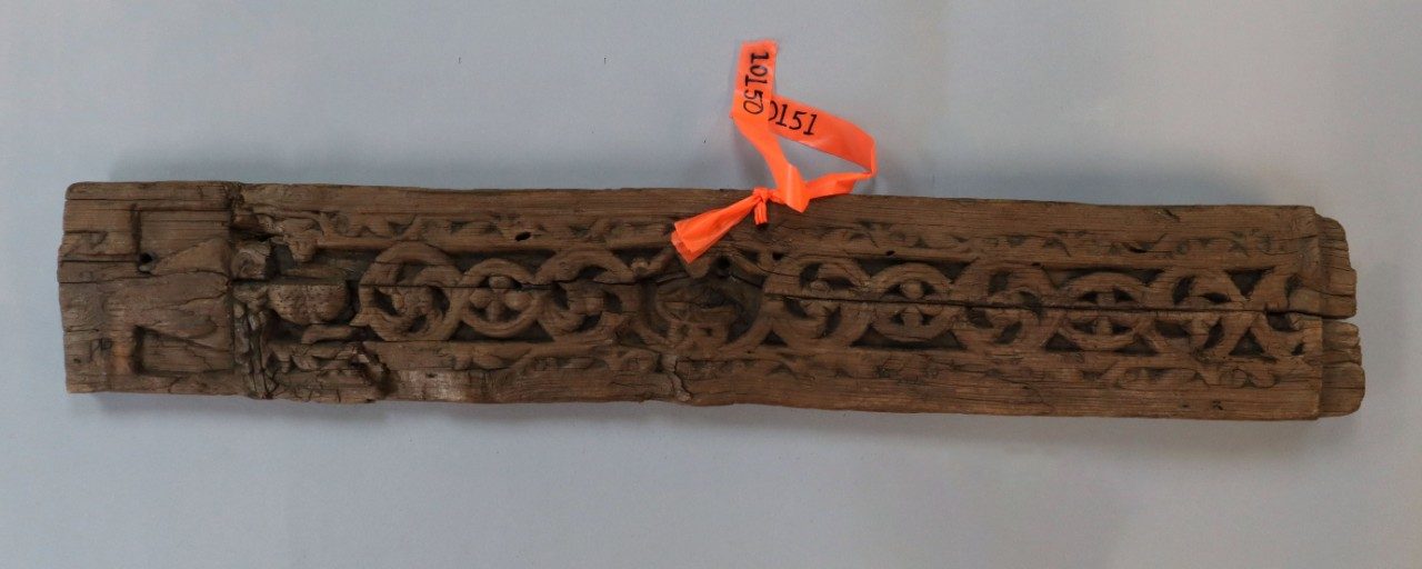 Long, rectangular wooden relief panel carved with a repeating pattern of interwoven vines and flowers.