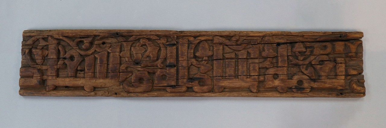 Long, rectangular wooden relief panel with Arabic inscription.