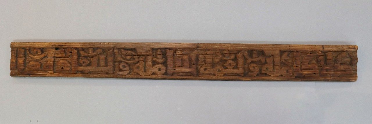 Long, rectangular wooden relief panel with Arabic inscription.