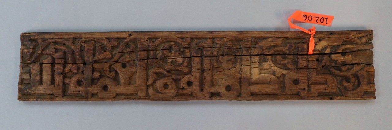 Long, rectangular wooden relief panel with Arabic inscription.