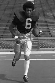 Archival photo of Dave Brown, wearing a number-6 jersey, running on a field with a football in his hand.
