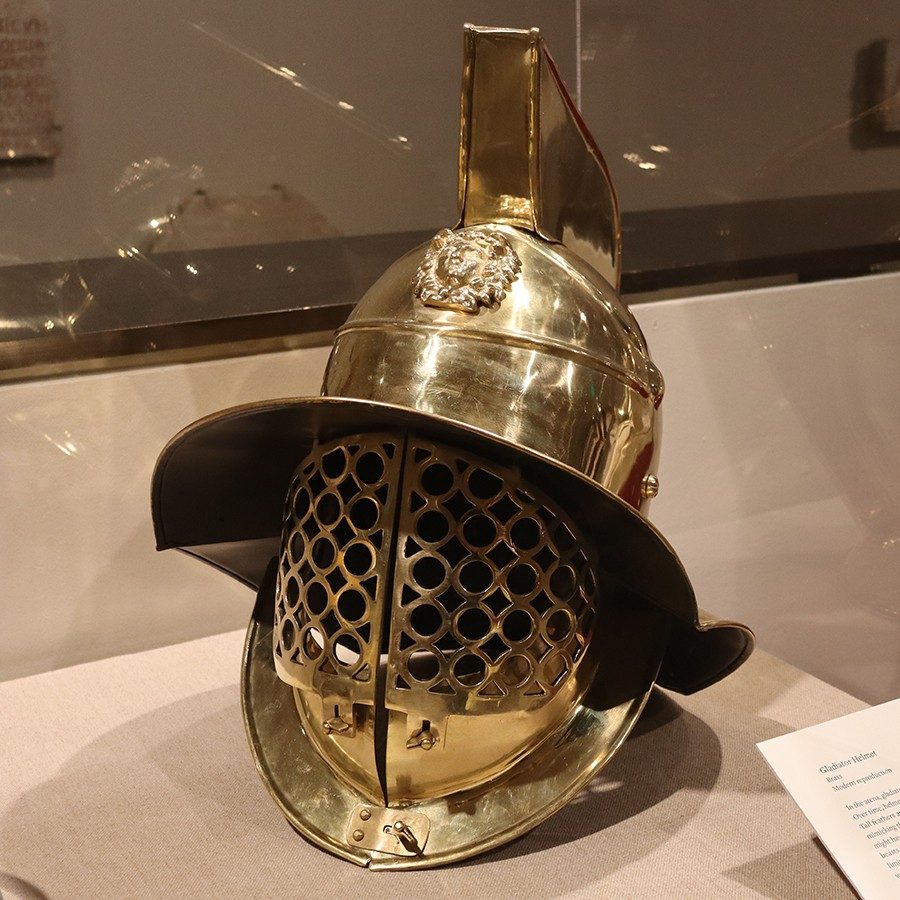 Brass helmet with a wide brim, an extensive face visor made of connecting circles, a collar, and a fin-like crest.