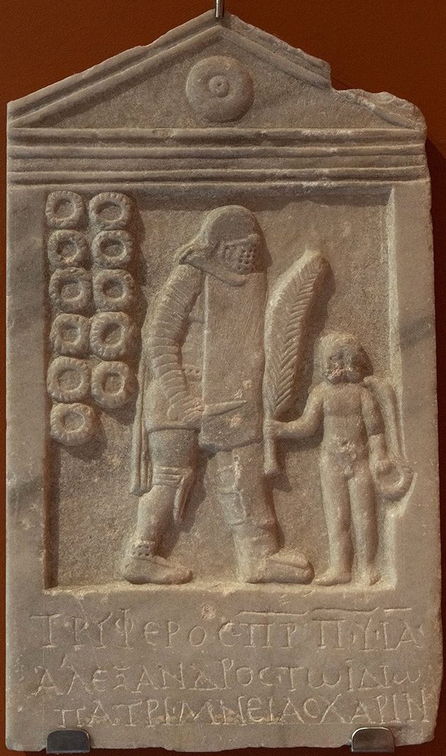 Marble tombstone showing a large figure of a gladiator in full armor. To his right are 11 circular rings. To his left is a smaller nude figure of Eros, holding a palm leaf, while three rows of Latin inscriptions are below.