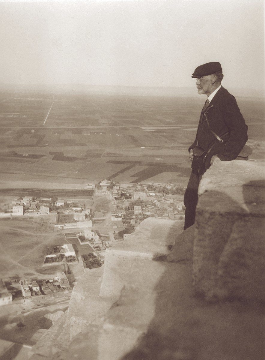 George Swain stands on the stacked stones of a pyramid looking out over a landscape of a city, with farmlands beyond.