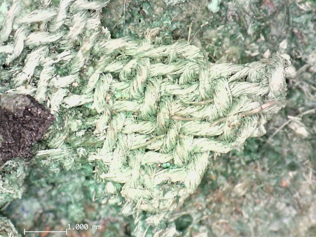 Close-up of the weaving patterns of an ancient, light green textile.
