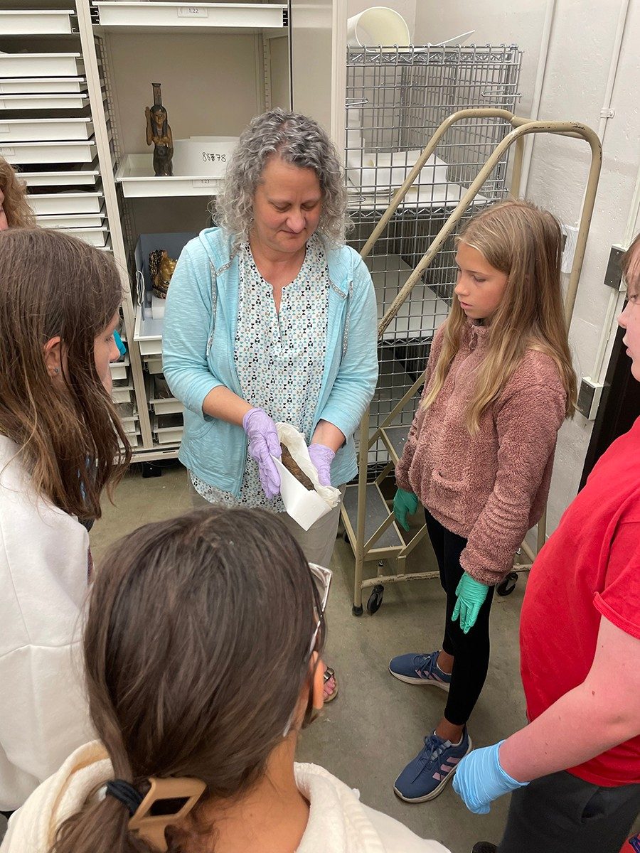 Kelsey Registrar Michelle Fontenot, with gloved hands, shows a group of middle-schoolers a hawk mummy.