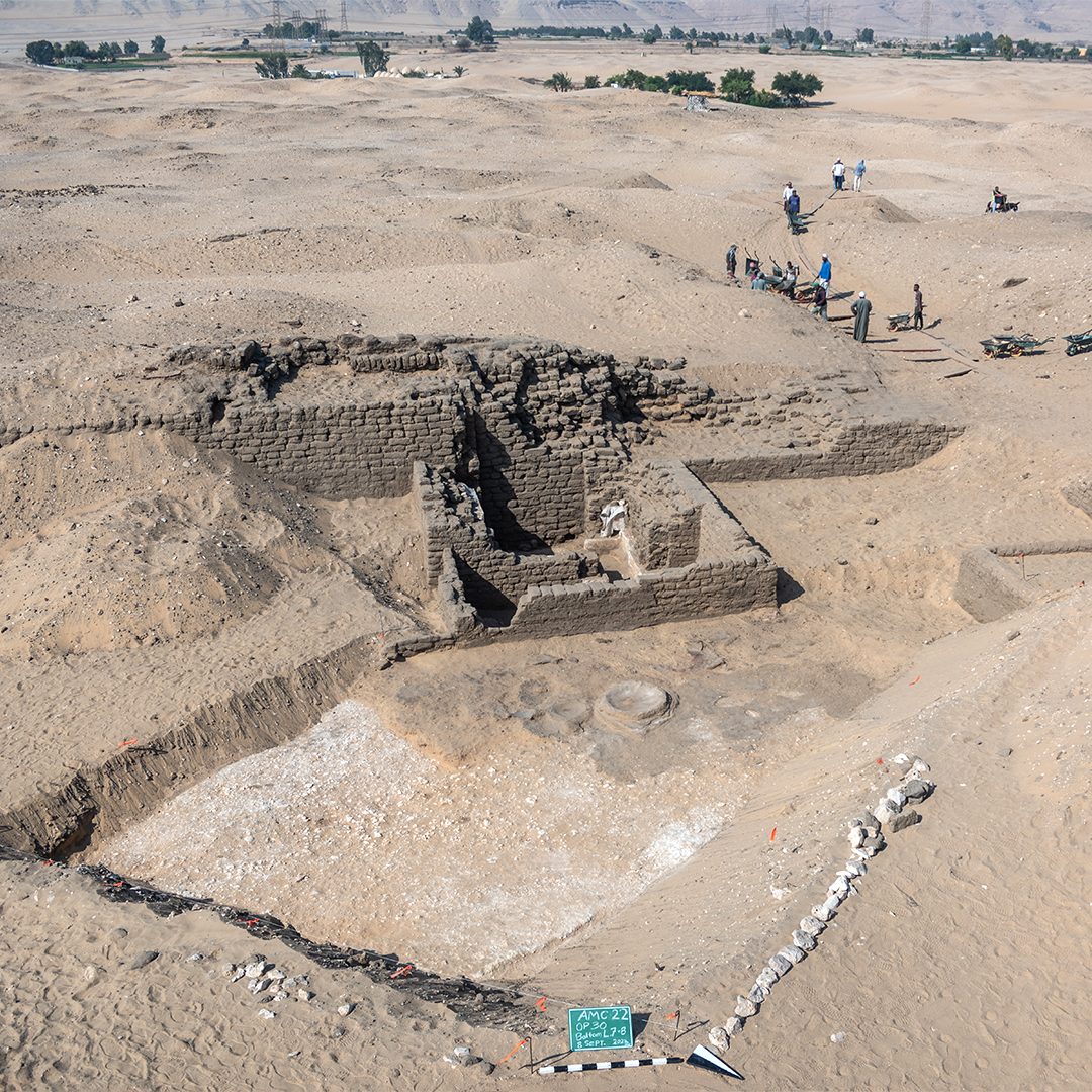 Aerial view of archaeological excavation at Abydos, Egypt, showing structure made of stacked bricks and workers in the background.