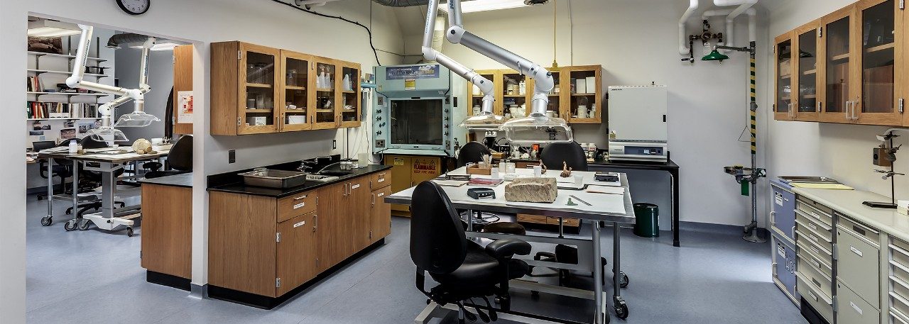 The conservation lab at the Kelsey Museum, featuring storage cabinets, vents, and artifacts on a table for study. 