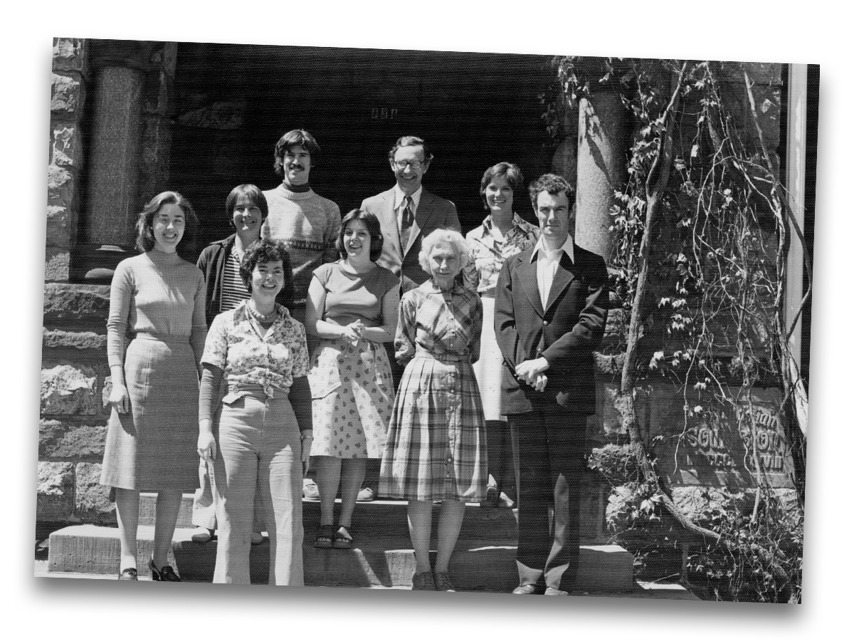 Archival photo of staff and curators at the Kelsey Museum, ca. 1970s. Nine individuals stand on the front steps of Newberry Hall.