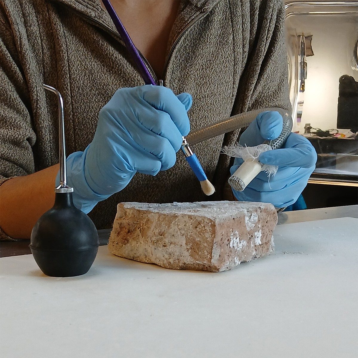Kathryn Peneyra holds a hose up to the surface of a stamped brick and lightly wipes away salt crystals with a brush.