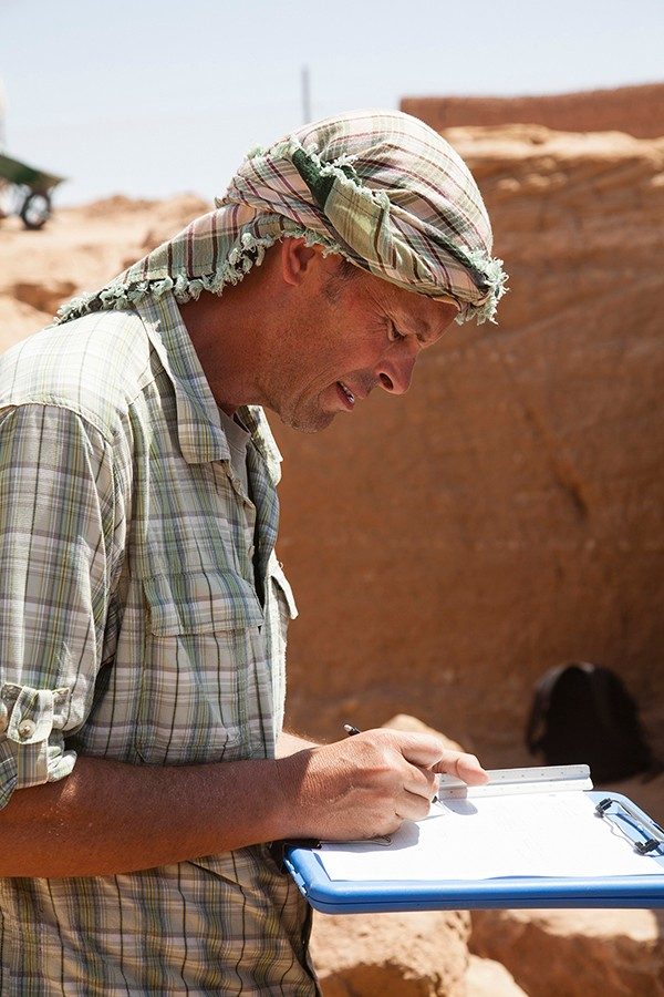 Geoff Emberling writing on a clipboard at an excavation site in Sudan.
