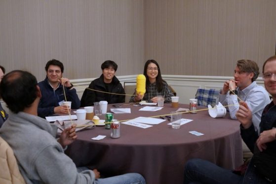 faculty and students at round table, one woman holding up a skein of yarn from the activity