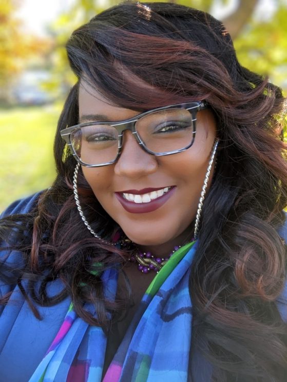 portrait of a Black woman smiling at camera wearing glasses, colorful blue scarf