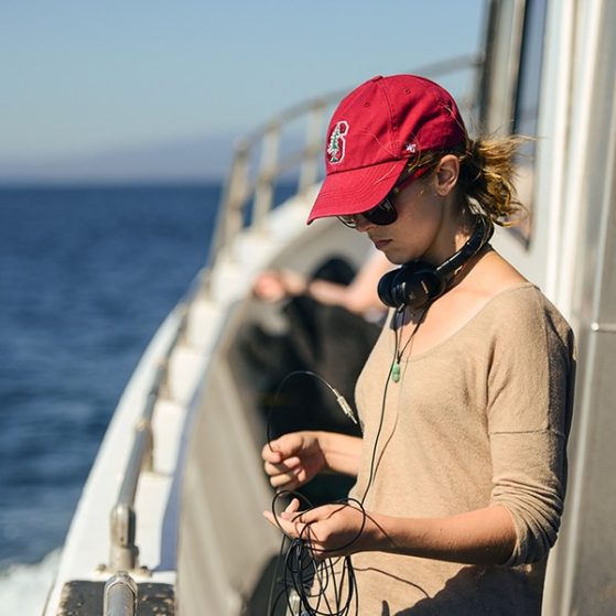 Woman next to railing on the deck of a boat wearing a red hat and headphones