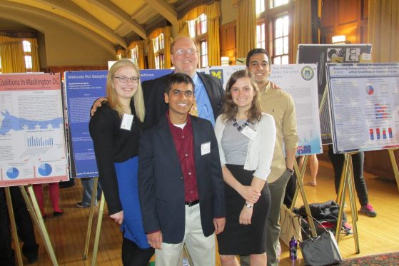 A group of OSers stand in front of an informational poster board for a presentation.