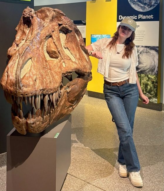Student Sophia Haynes stands with arm on T-Rex skull