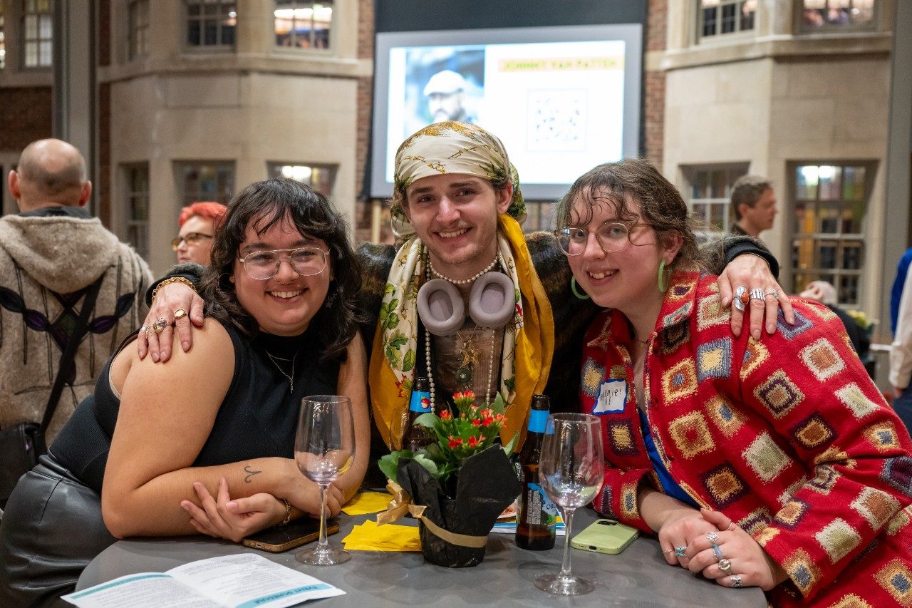Group of three people in colorful outfits posing together at a table with their arms around each other