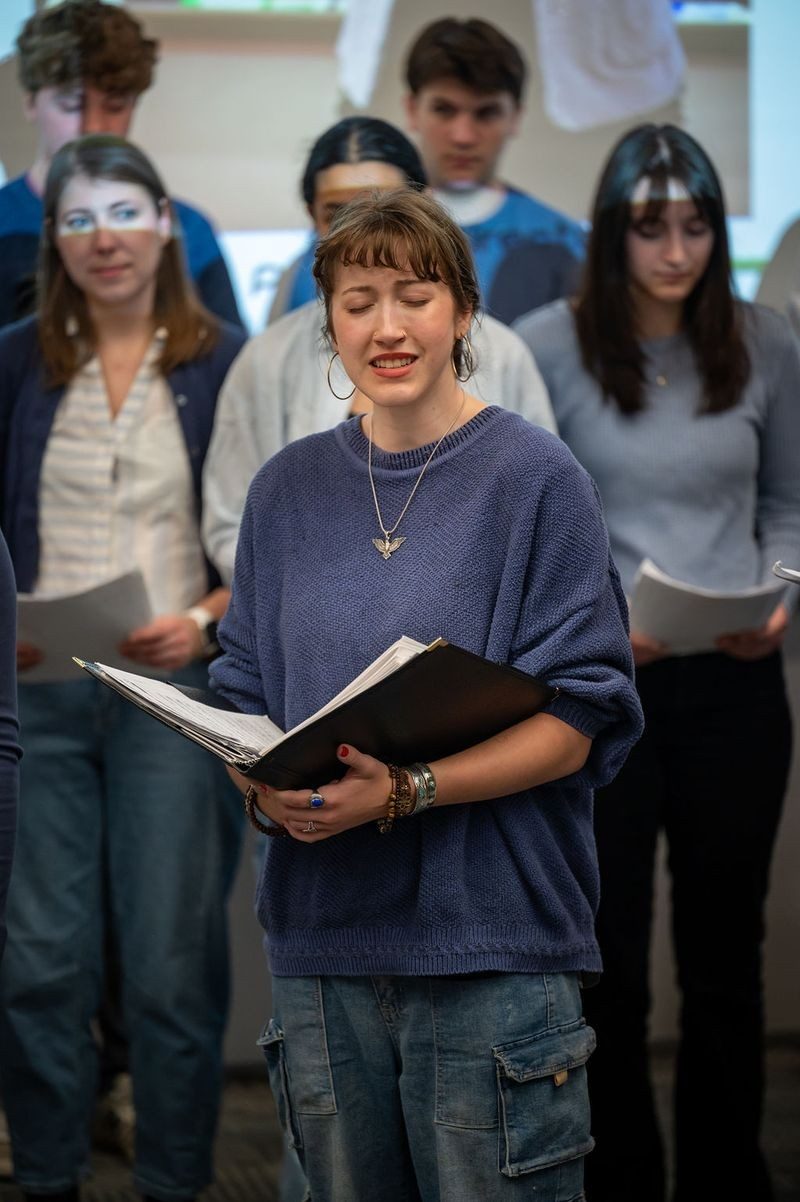 Woman standing with eyes closed, holding an open book with people in the background