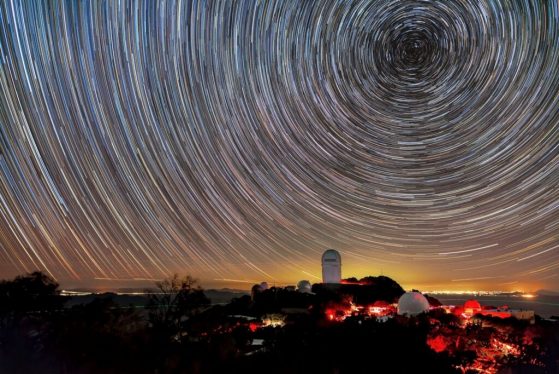 The Dark Energy Spectroscopic Instrument mounted on the U.S. National Science Foundation’s Nicholas U. Mayall 4-meter Telescope at Kitt Peak National Observatory at night with the swirling universe above