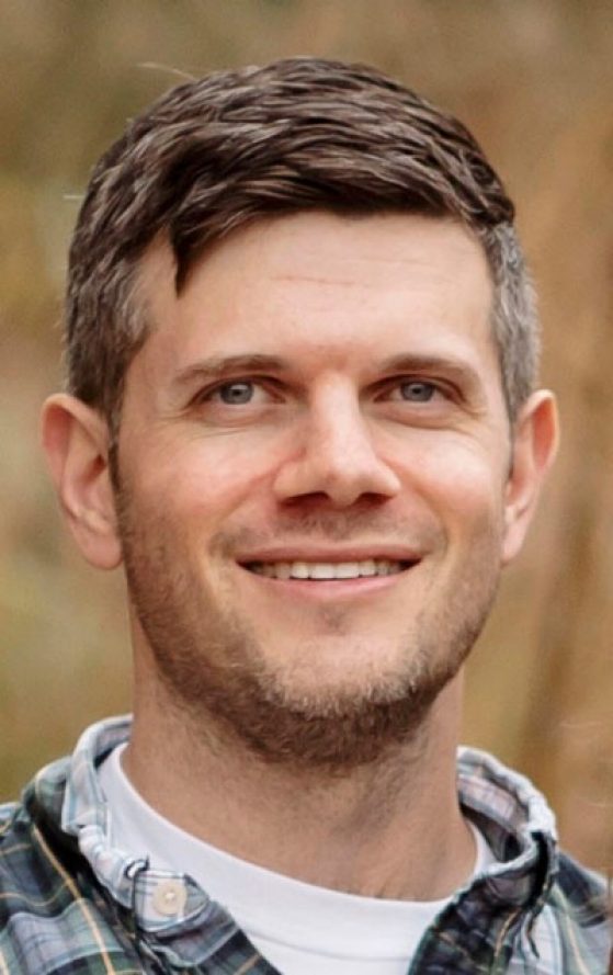 Professor Joshua Spitz in a white shirt and green and blue plaid overshirt.