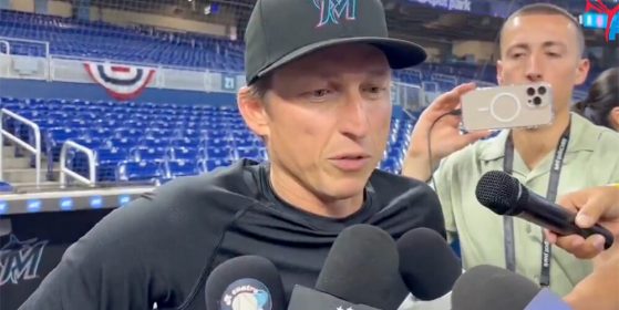 a man with a Marlin's baseball cap in a black t-shirt being interviewed by reporters.
