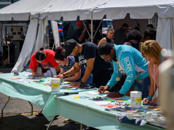 five people stand at tables painting together in a street art fair
