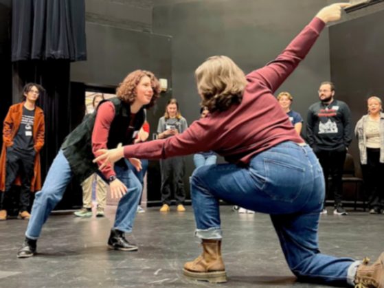 two students on stage face each other in improv workshop