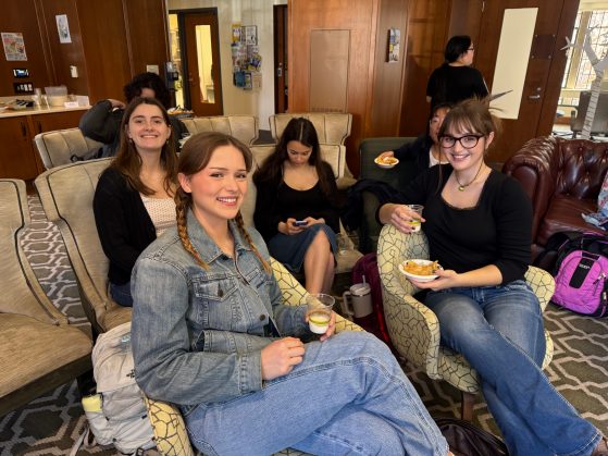 Four female students sit in a lounge and smile at the camera