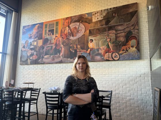 A young woman poses in front of her mural with arms crossed