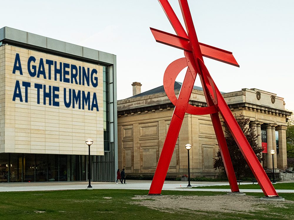 A large piece of artwork sits outside in front of the University Museum of Art. On the building it says "A Gathering at the UMMA"