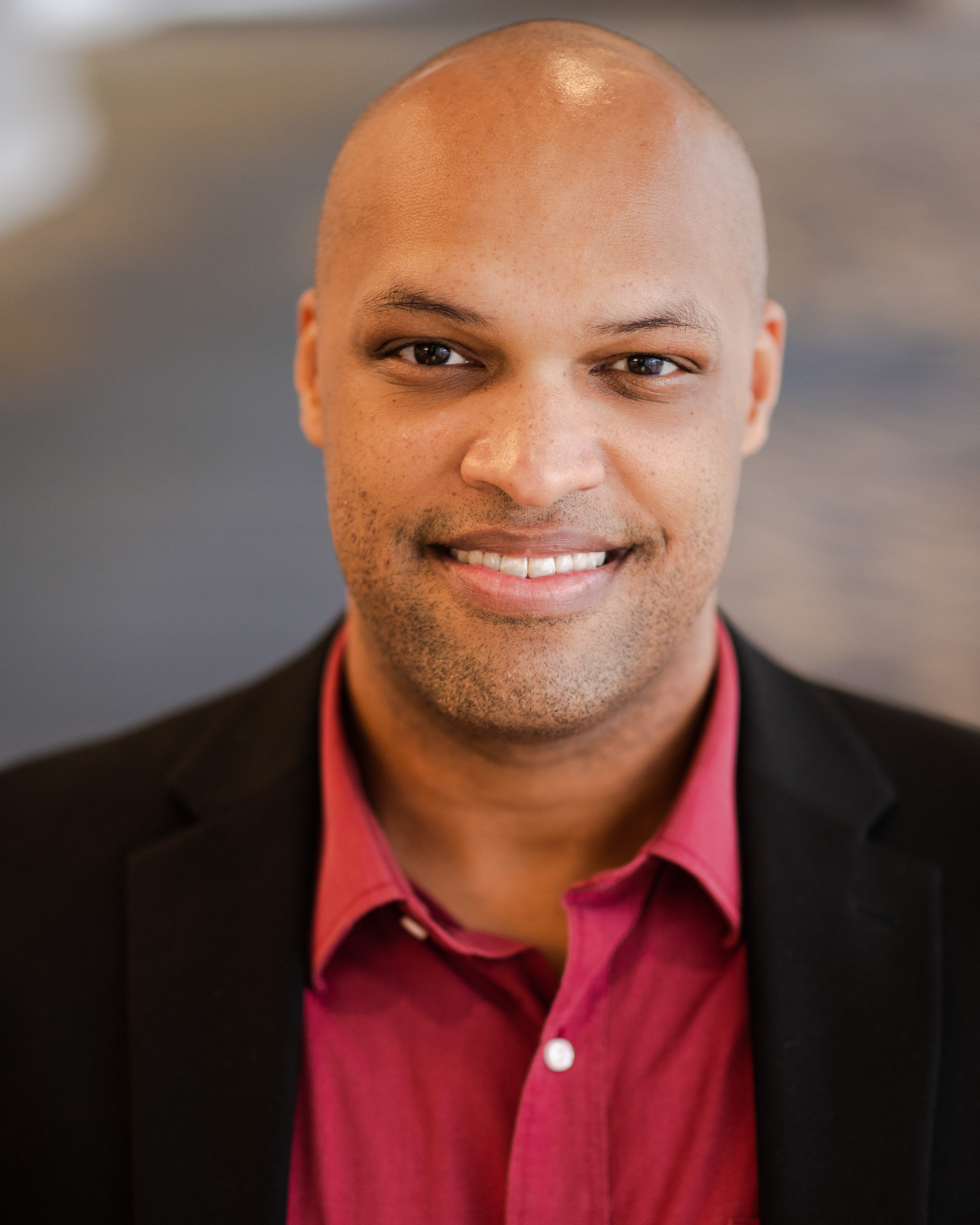 Headshot of LJ Randolph wearing a black jacket and colored shirt
