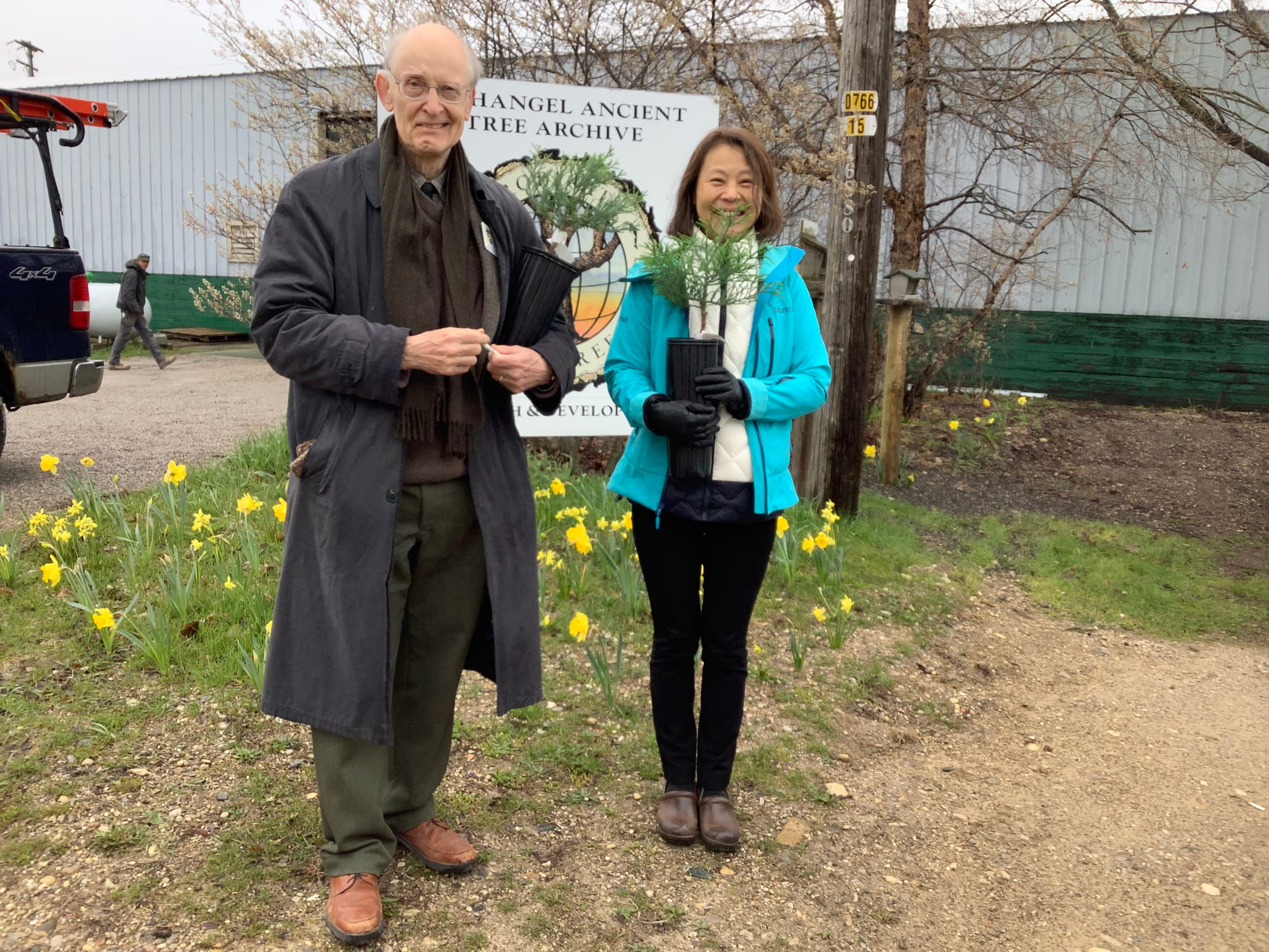 Two professors standing holding small trees outside