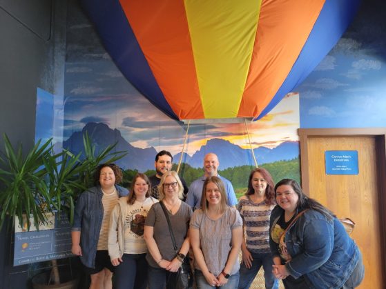 The SLC Team at their team building event, pictured in front of an indoor hot air balloon with a mountainscape backdrop