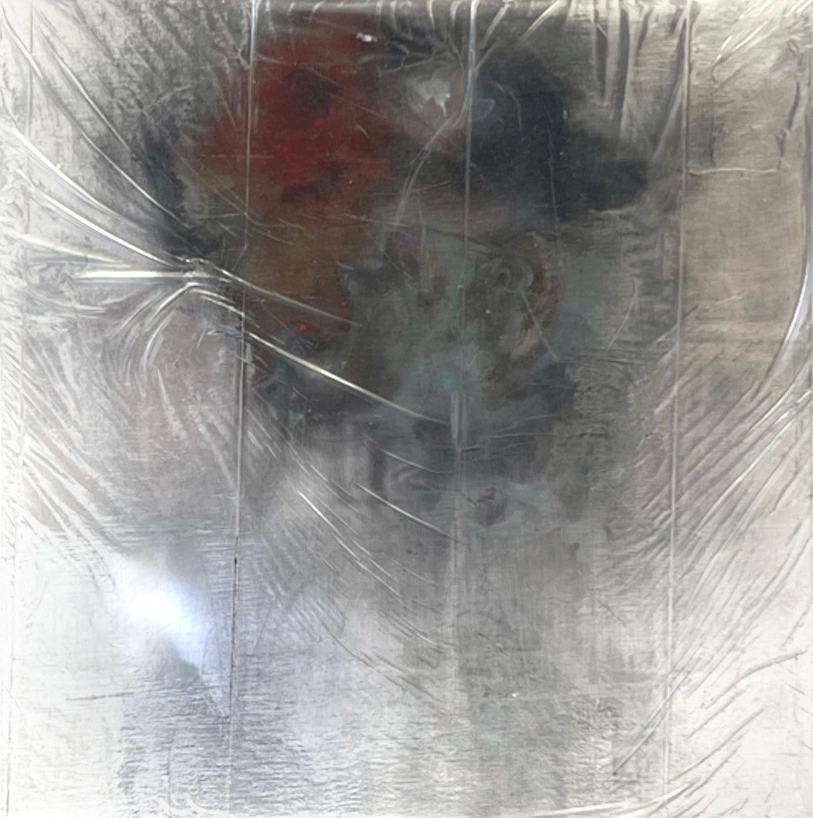 abstract art with a wrinkled silver surface and black and reddish area at the top of the frame that appears to be a face emerging