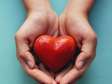 Top view of both hands holding red hearts on a blue background, as a symbol of care and compassion. Template design with copy space for add text.
