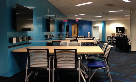 An empty team-based learning space: Multiple chairs at multiple tables, each with a wall-mounted display