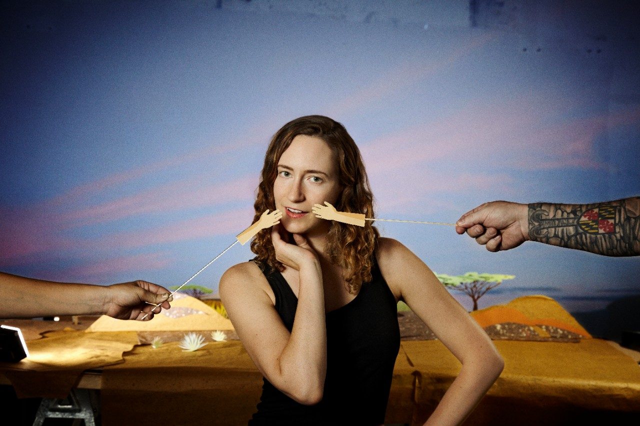 Person with hand puppets touching her face